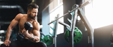 Strong muscular man with naked torso doing exercises with dumbbells, working out in gym, free space photo