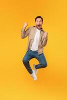 A man with a beard and casual clothing leaps into the air, his fists clenched and mouth open in a shout of exhilaration against a yellow backdrop that radiates a sense of energy and happiness. photo