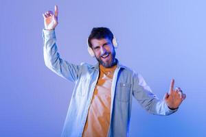 A young man enthusiastically dances to music, wearing headphones, in a vibrant, colorful room during nighttime. He looks happy and energetic. photo