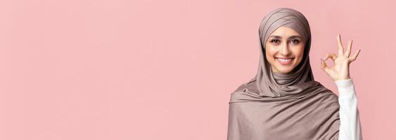 Everything is ok. Happy islamic woman in hijab showing ok gesture over pink background in studio, free space photo