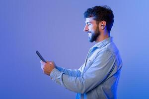 A man is seen holding a cell phone in his hand, looking at the screen. He appears focused on the device, possibly typing or scrolling through content. His hand grips the phone firmly. photo