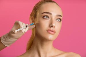 A close-up photo of a woman receiving a facial injection treatment. The woman is looking up and has a serious expression. The injection is being administered by a gloved hand
