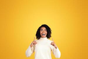 Place For Ad. Portrait of happy black girl pointing fingers up at copyspace isolated over yellow background, vertical image photo