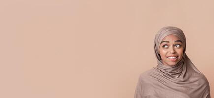 Portrait of doubtful black muslim woman in headscarf biting lip and looking away at free space over yellow background, unsure about something photo