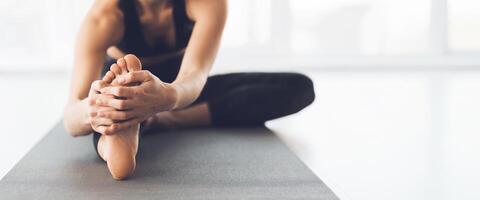 A person performs a seated toe stretch on a yoga mat in a well-lit studio, focusing on flexibility and relaxation, cropped, copy space photo