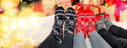Christmas atmosphere background. Three pairs of feet in warm socks with winter holiday print ornament, panorama photo