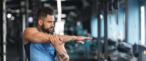 Sporty man at gym doing stretching exercises for hands, empty space, web-banner photo