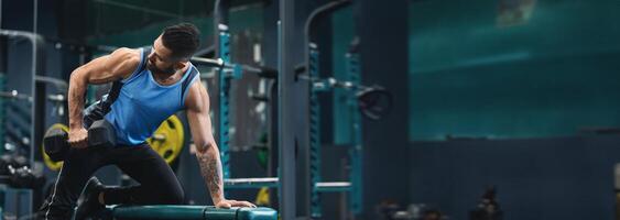 A man performs a strength training exercise with a dumbbell at a gym, focusing on building muscle and improving fitness, copy space photo