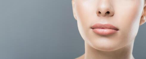 A woman face is shown in a close-up, highlighting her clear, smooth skin and neutral lip color. The background is a plain gray, cropped, copy space photo