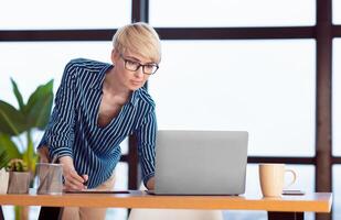 Successful Business Lady Using Laptop Taking Notes Standing Near Table In Modern Office. Selective Focus, Empty Space photo