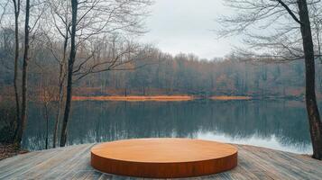 Early morning light casts a soft glow on a circular wooden platform by a serene lake, with bare trees reflecting on the still water's surface, highlighting the peaceful autumn landscape. photo