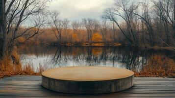 A circular concrete platform sits on wooden decking, overlooking a calm lake surrounded by trees displaying autumn colors. This serene location invites reflection and connection with nature. photo