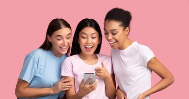 Cool App. Three Millennial Girls Using Smartphone Showing And Recommending Mobile Application To Friends Standing Over Pink Background photo