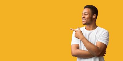Special Offer. Portrait of half-turned afro guy pointing aside at copyspace with index finger. Panorama, orange wall photo