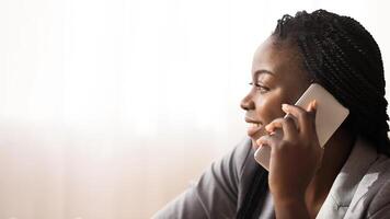 In touch. Profile portrait of smiling african american woman talking on cellphone with somebody against window background, copy space photo