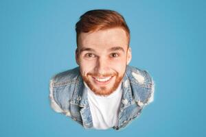 Above portrait of funny millennial redhaired guy, smiling upwards at camera, blue background, studio photo