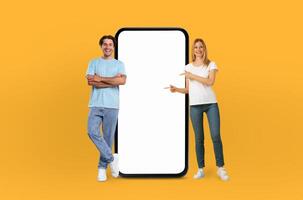Young couple smiles are infectious as they stand side by side, presenting a large smartphone with a pristine, empty screen, ready to capture the imagination. photo