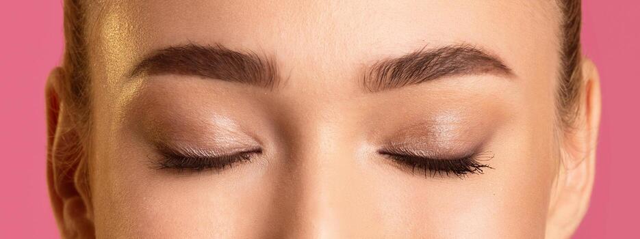 This image shows a close up of a woman eyelids, with defined eyebrows and subtle eye makeup. The photo is taken from a low angle, focusing on the upper eyelids and brow bones.