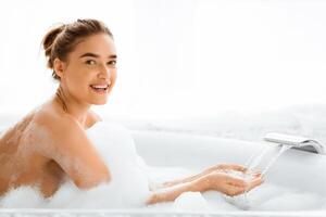 Woman enjoying warm bath and checking temperature of running water, smiling to camera photo