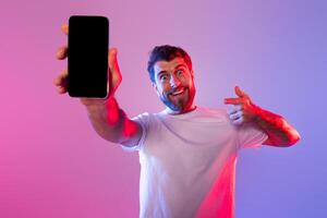 A man wearing a white shirt is standing while holding a cell phone in his hand. He appears to be looking at the screen of the phone with a focused expression, mockup photo