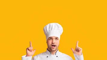 Look There. Cook Man Pointing Fingers Up Posing Over Yellow Background. Studio Shot photo