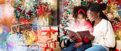Christmas fairy tale. Pretty young african mother reading magic book to her daughter near Xmas tree, looking at shining pages with excitement photo