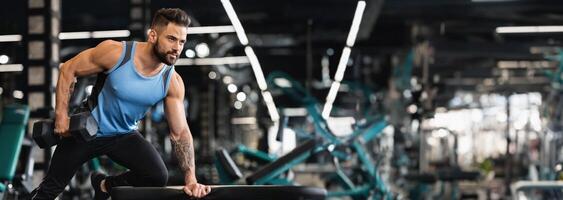 Millennial muscular man working out in gym, doing exercises with dumbbells at biceps, free space photo