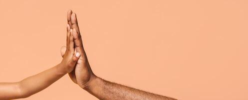 A close-up image of two hands giving a high five. The hands are both brown and the background is a soft peach color. The image captures the simple act of connection and celebration. photo