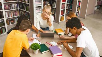 Multinational students gathering in circle, making homework together in library, using laptop photo