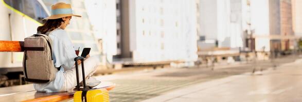Millennial caucasian lady with backpack, suitcase, passport and ticket looks at phone with empty screen, waiting for transport on train station or airport, copy space photo
