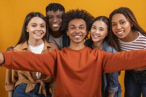 A group of five friends are taking a selfie. They are all smiling brightly and looking directly at the camera. They are standing close together in a casual pose, suggesting they are close friends. photo