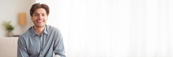 Cheerful Handsome Young Man Smiling At Camera Sitting On Couch At Home. Empty Space For Text, Web-banner photo