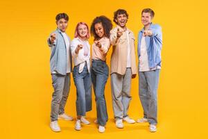 Five young adults stand in a line, pointing their index fingers toward the camera. They all smile at the camera, exuding a sense of camaraderie and unity. photo