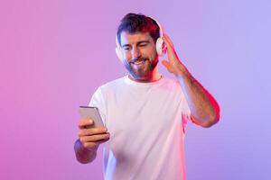 A man is sitting and listening to music through headphones while holding a cell phone in his hand. He appears focused on the music playing and the content on his phone screen. photo