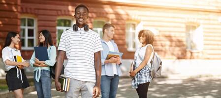 Education grants concept. Portrait of happy african student guy posing in university campus with classmates on background photo