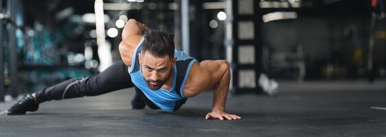 Strength exercise. Muscular man doing push ups on on hands in gym, panorama with copy space photo