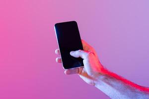 A person holds a smartphone with a dark, unlit screen against a gradient purple background. The lighting casts a soft, ambient glow, creating a modern and tech-savvy atmosphere. photo