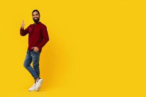 Indian man is standing in front of a bright yellow background, smiling and giving a thumbs up gesture. The man appears confident and happy, with a clear expression of approval, copy space photo
