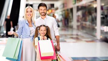 A young family, consisting of a father, mother, and daughter, are smiling and carrying shopping bags while standing in a modern shopping mall, enjoying their shopping trip, copy space photo