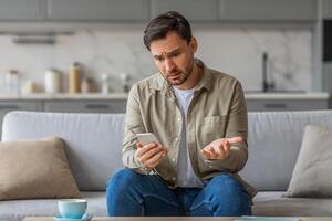 A man sits on a couch in his living room, holding his phone with a confused expression on his face. He gestures with his other hand, as if trying to explain or clarify something. photo