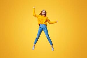 Euphoric teen girl jumping in air with hands up, orange studio background with empty space photo