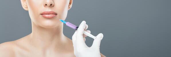 A professional in a clinic setting administers a cosmetic injection near a woman lips, aiming for lip enhancement. The practitioner wears a white glove and wields a syringe, cropped, copy space photo