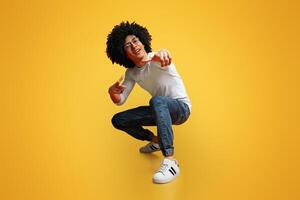 Hey you. Cocky millennial guy pointing at camera, making challenge, squatting on orange studio background photo