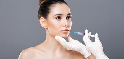 A woman is receiving a dermal filler injection administered by a professional. She sits calmly as a gloved hand holds the syringe near her face, emphasizing a meticulous and sanitary procedure. photo