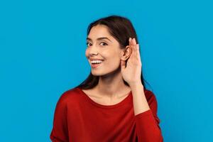A woman with a joyful expression on her face is smiling and touching her ear with her hand, indicating she might be listening or adjusting an earpiece. She appears content and engaged in the moment. photo