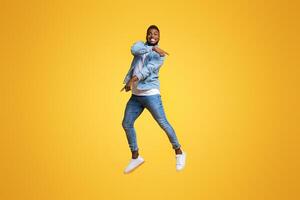 Look there. Funny african american man jumping in air and pointing at copy space over yellow studio background. photo