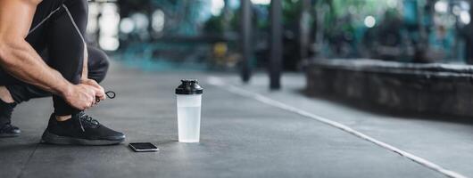Man tying shoe laces on sneakers in gym, preparing for workout, empty space, cropped photo
