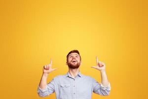 A man standing with hands in the air in front of a bright yellow background, pointing at copy space above him photo