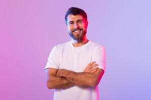 A man is standing with his arms crossed in front of a solid purple background. He appears confident and assertive in his posture. photo