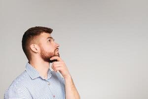 Portrait of thoughtful guy posing isolated on beige studio background, touching his chin, panorama, copy space photo
